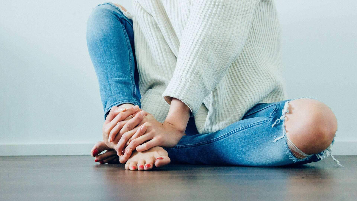 شخص يرتدي بنطال جينز أزرق ممزق مع ركبة متآكلة وجينز أزرق ممزق مع ركبة متآكلة وسترة كريمية مطرزة بأضلاع، جالسًا متربعًا على الأرض.